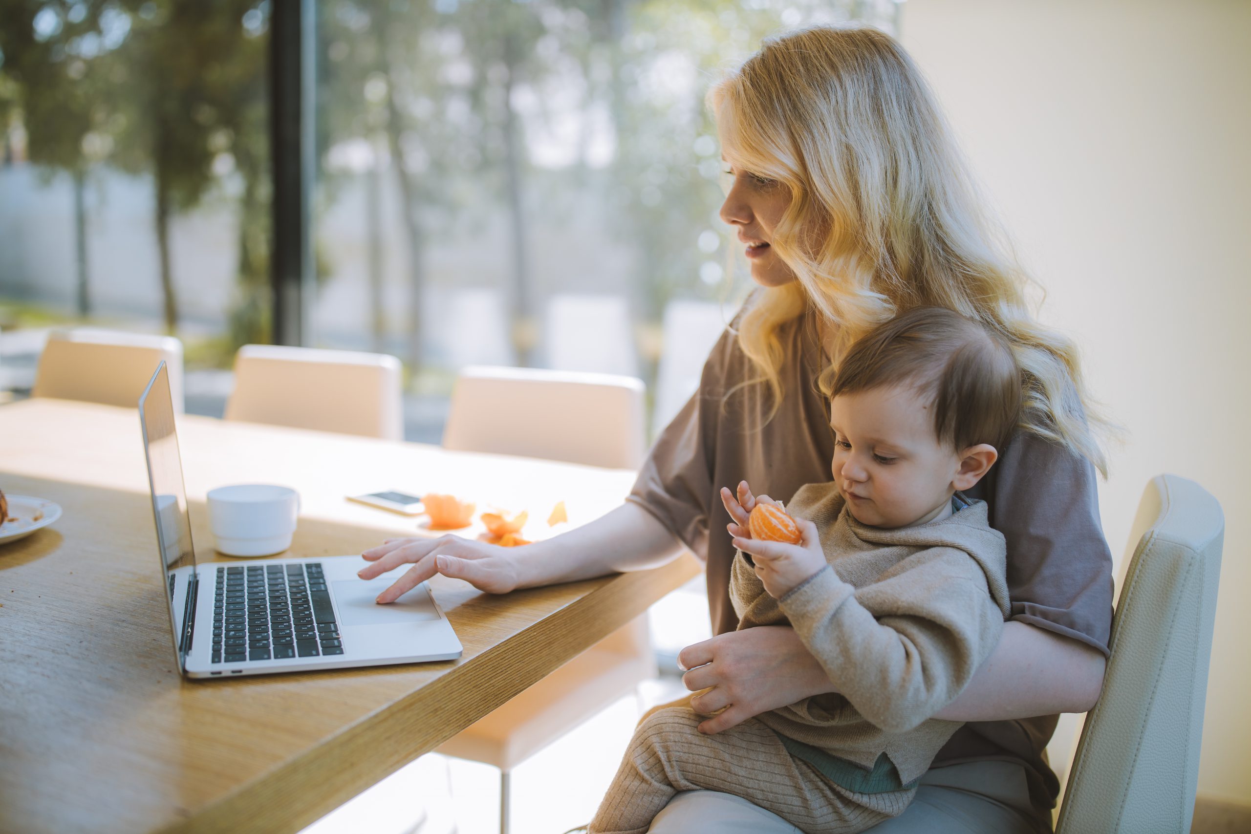 Woman holding baby while working on laptop.